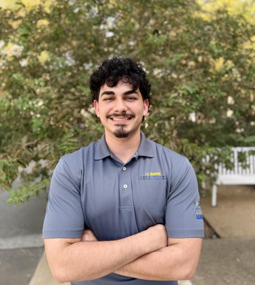 Smiling young man with arms crossed outdoors in gray polo