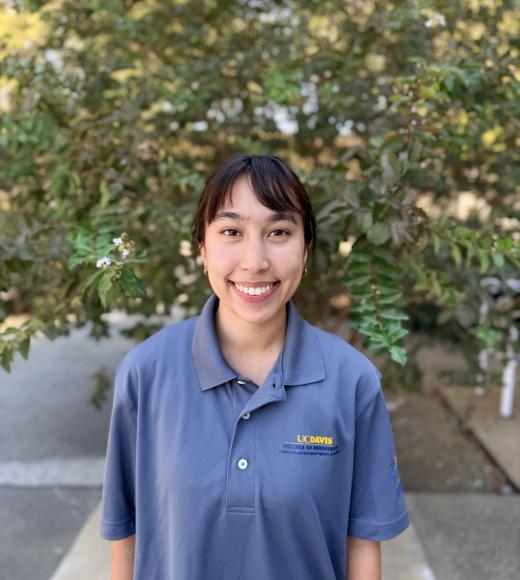 Smiling young woman in blue polo with logo, blurred leafy background