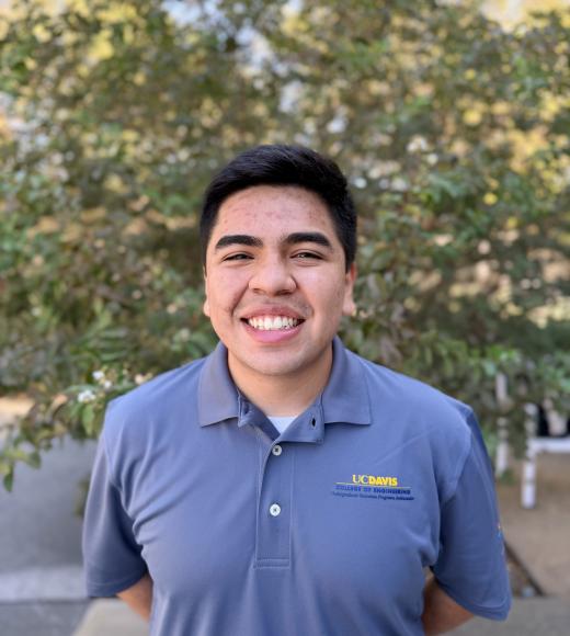 Smiling young man in blue polo with small logo, outdoor portrait against trees